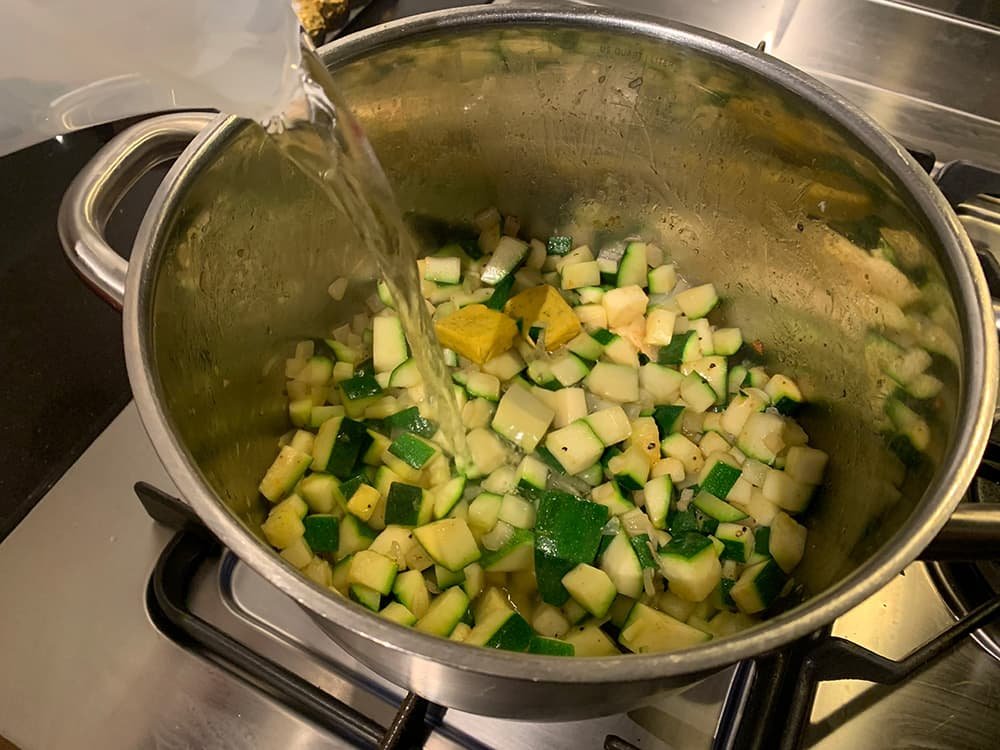Voeg bouillonblokjes toe, schenk het water erbij en laat de soep 15 minuten zachtjes koken, tot de courgette gaar is.